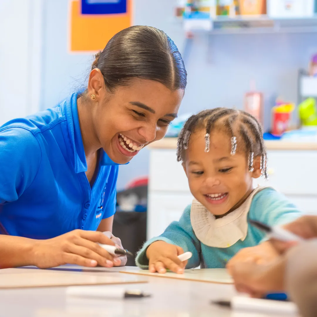 Teacher helping a child draw at a classroom table