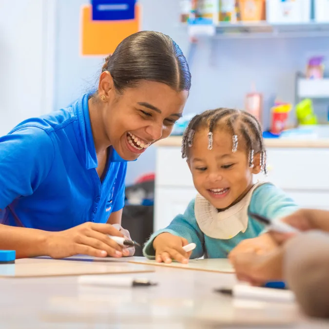Teacher helping a child draw at a classroom table
